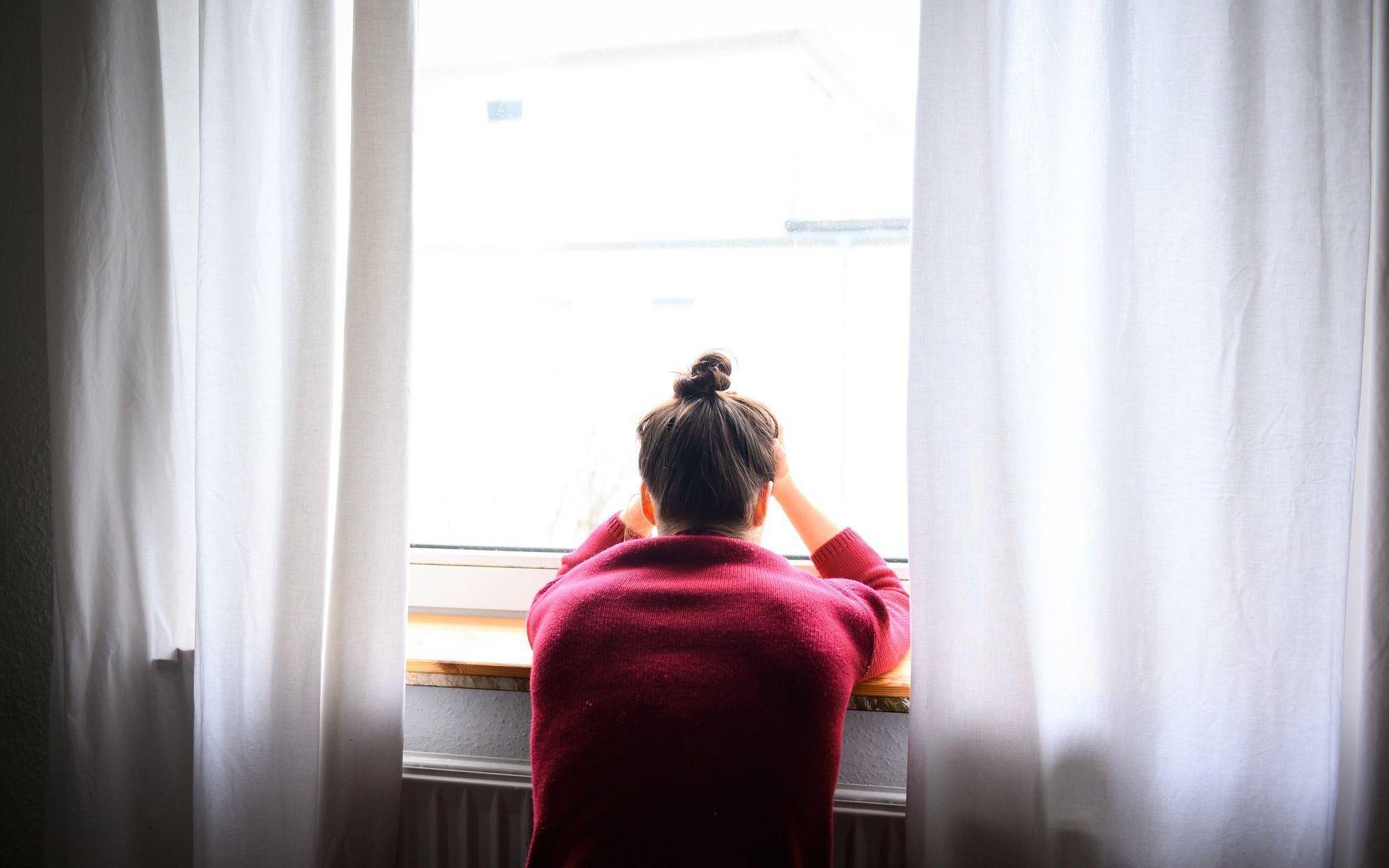 Frau sitzt mit Kopf in den Händen am Fenster