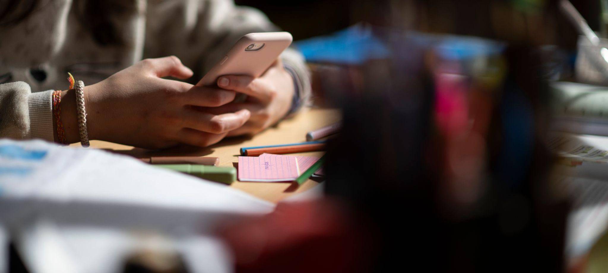 Eine Jugendliche sitzt mit Smartphone an einem Schreibtisch
