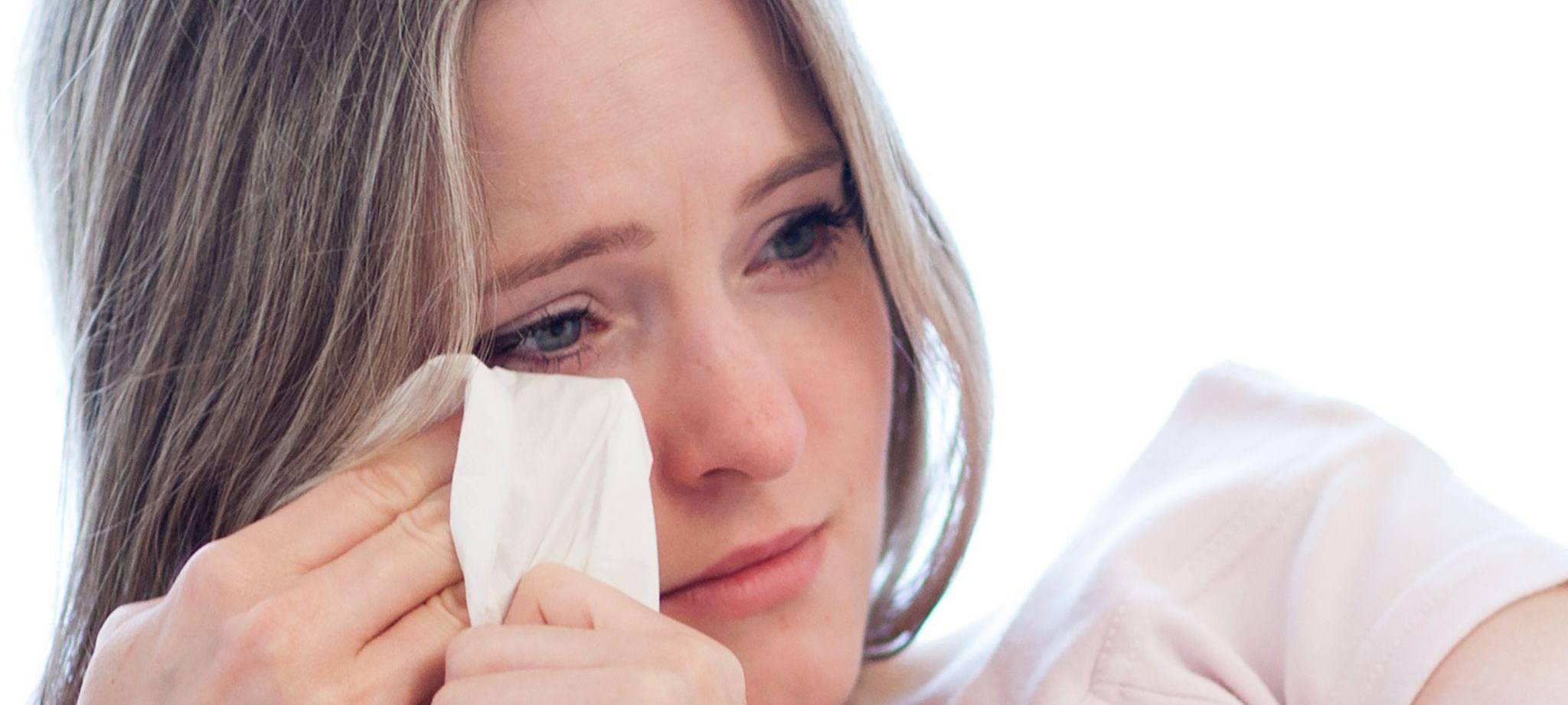 Frau wischt sich mit einem Taschentuch die Tränen aus den Augen
