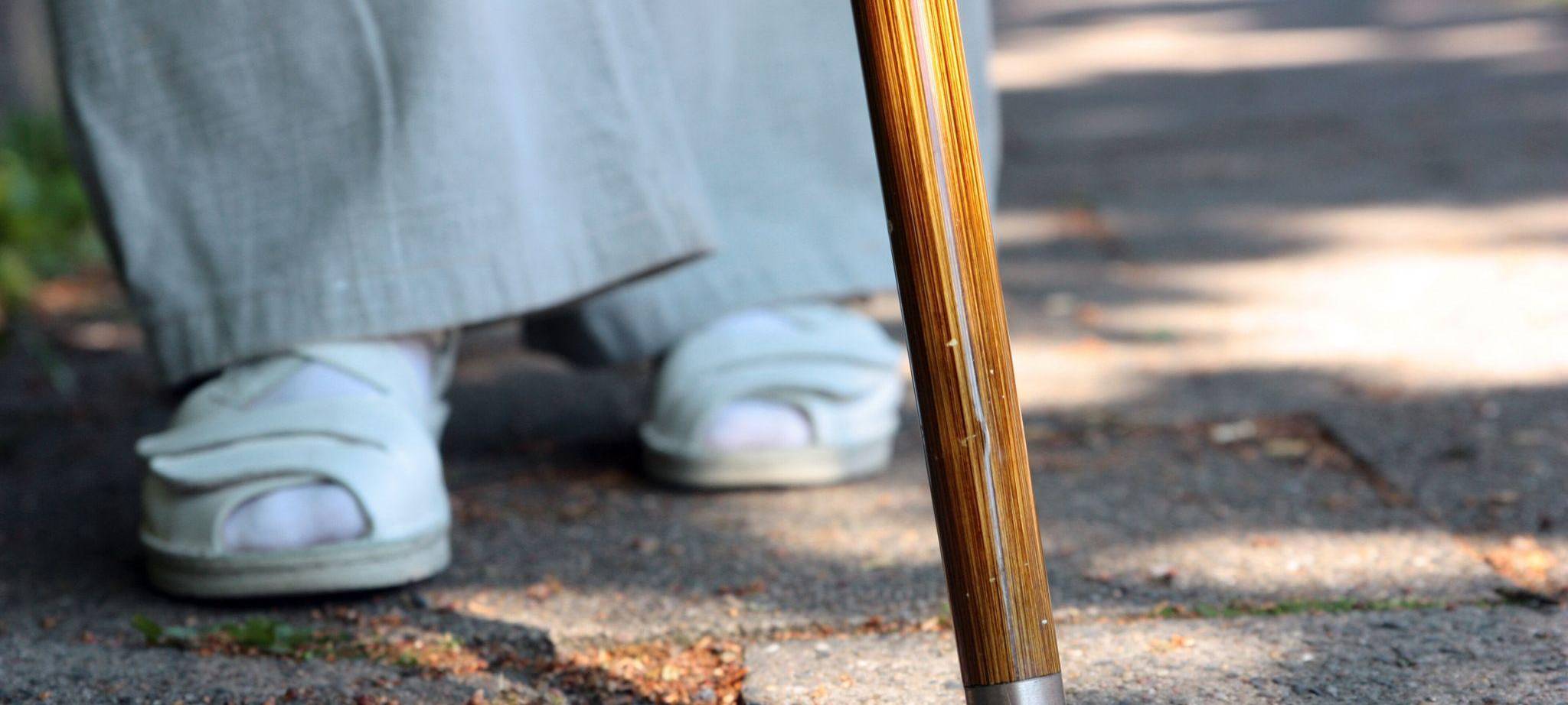 Eine Frau steht mit einem Stock auf einem Gehweg