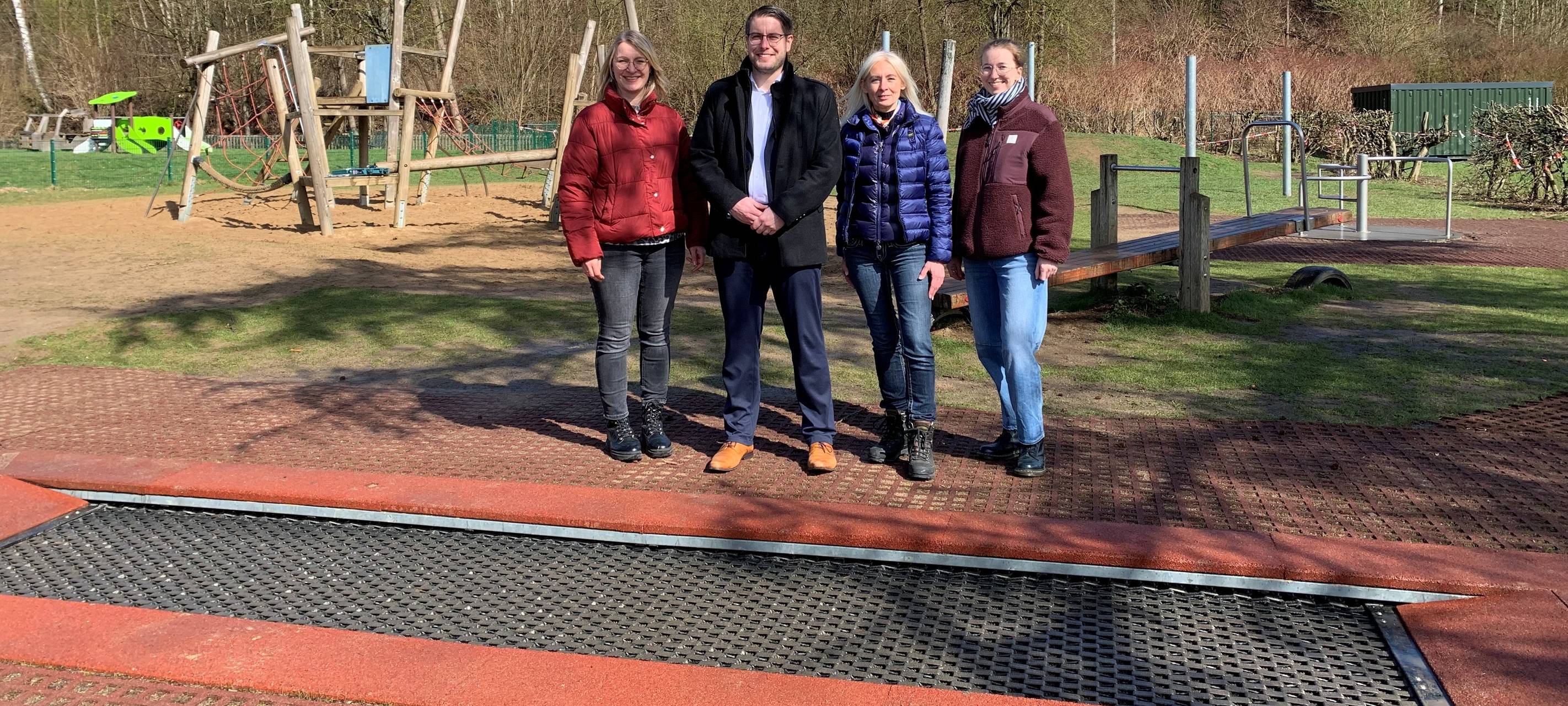 Bürgermeister Michael Kolodzig mit der städtischen Planerin Sarah Severine Höfer, Schulleiterin Claudia Gawrosch und Konrektorin Anna-Lena Nies (v.l.) von der Friedrich von Bodelschwingh-Grundschule Buschhütten am Inklusionstrampolin. Hinten rechts im Bild sieht man zudem das Inklusionskarussel.