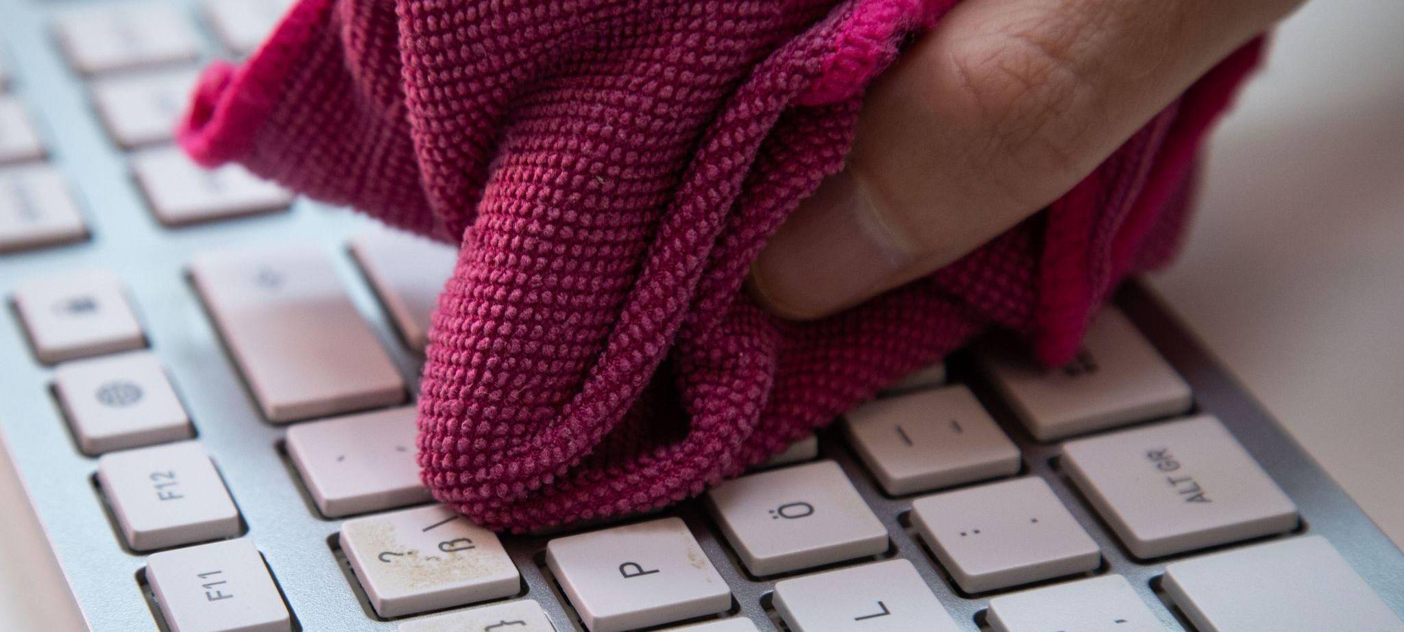 Ein Mann reinigt eine Tastatur mit einem Mikrofasertuch
