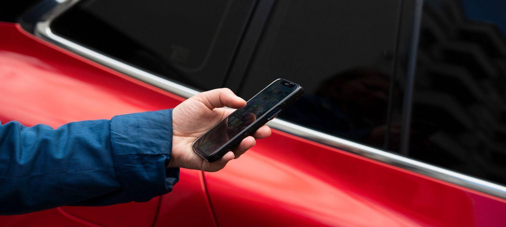 Mann steht mit seinem Smartphone vor einem Auto