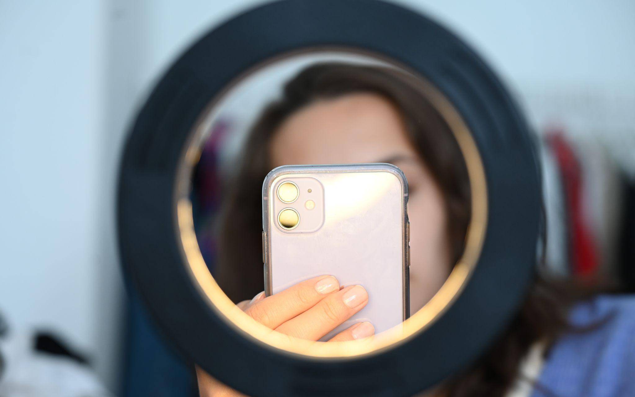 Influencer sitzt mit dem Smartphone hinter einem Ringlicht