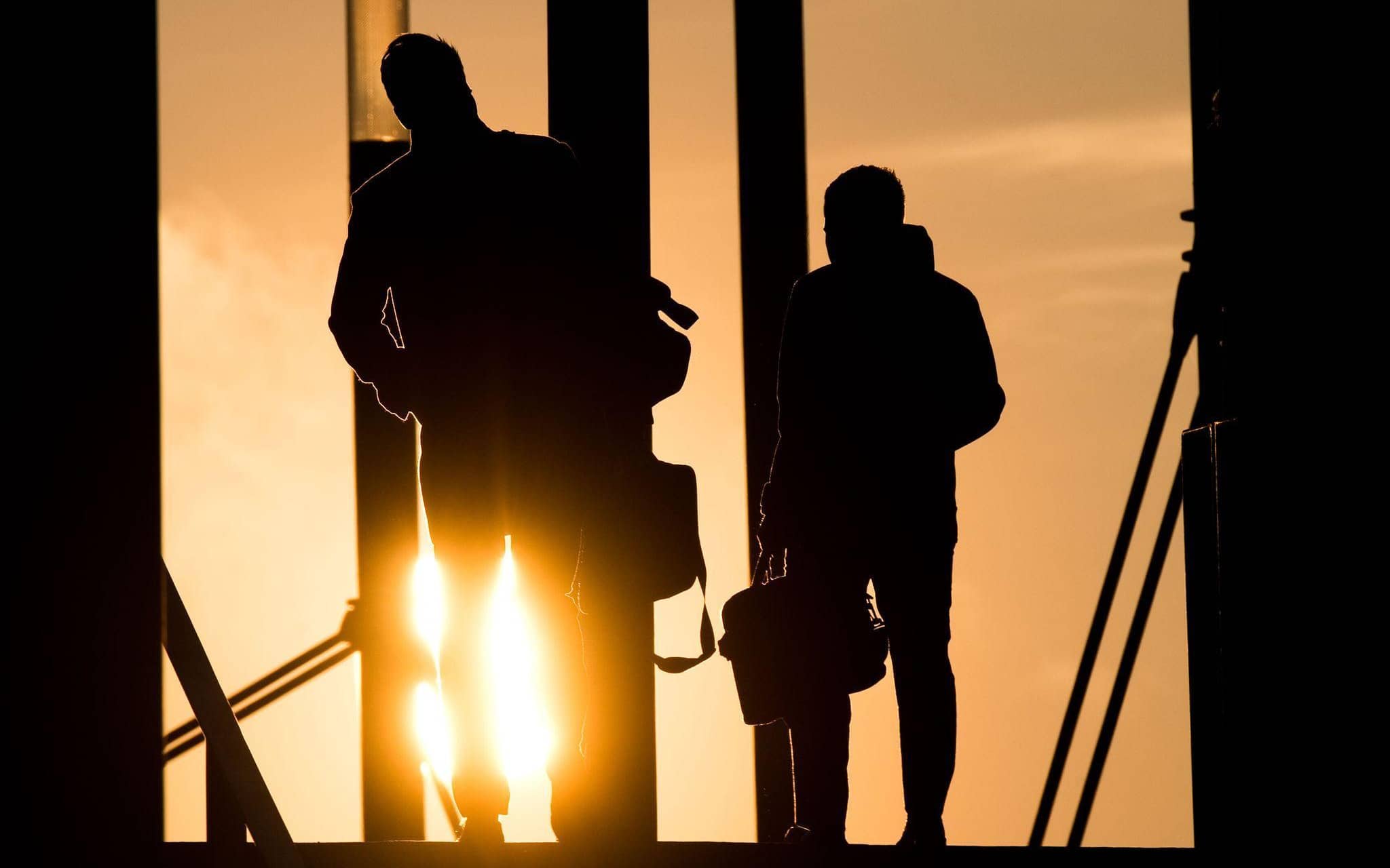 Zwei Männer gehen mit Aktentasche bei Sonnenaufgang über Brücke